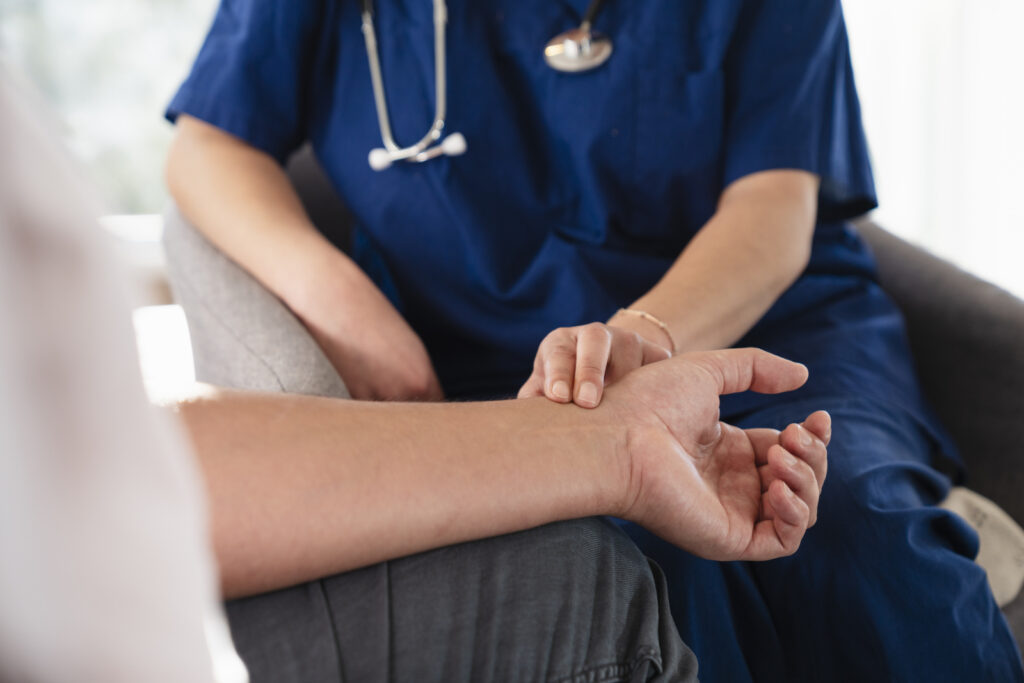 Nurse takes a man's pulse at a check up after a stroke and suspected carotid artery disease.