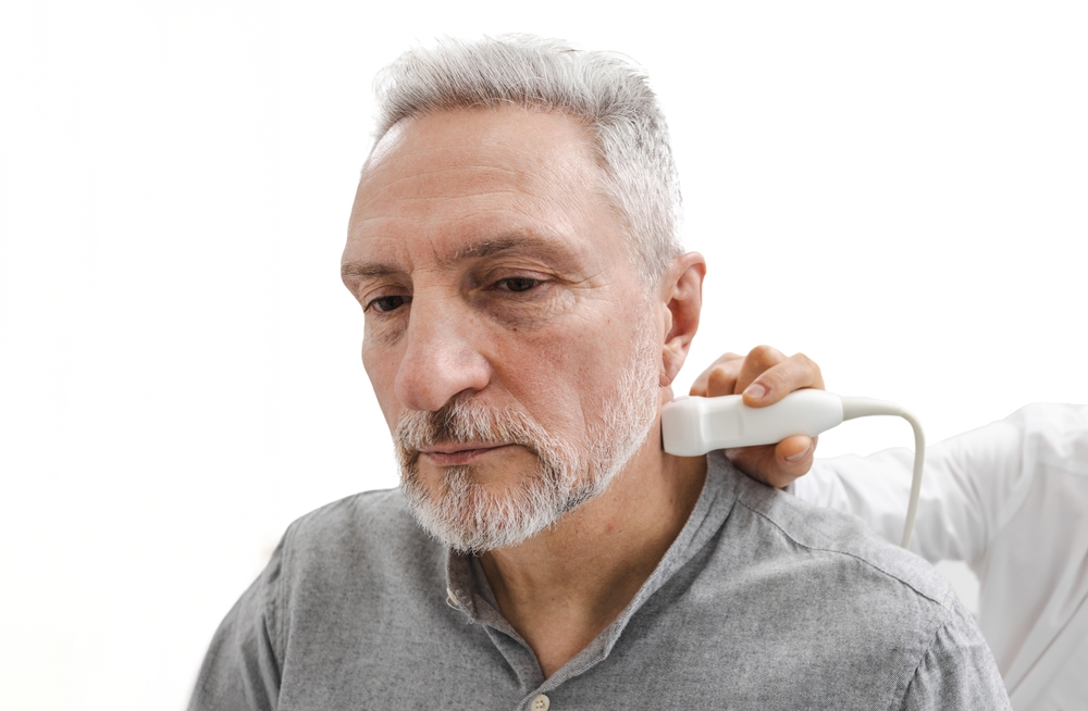 Vascular doctor or specialist scans carotid arteries on the side of an older man's neck.