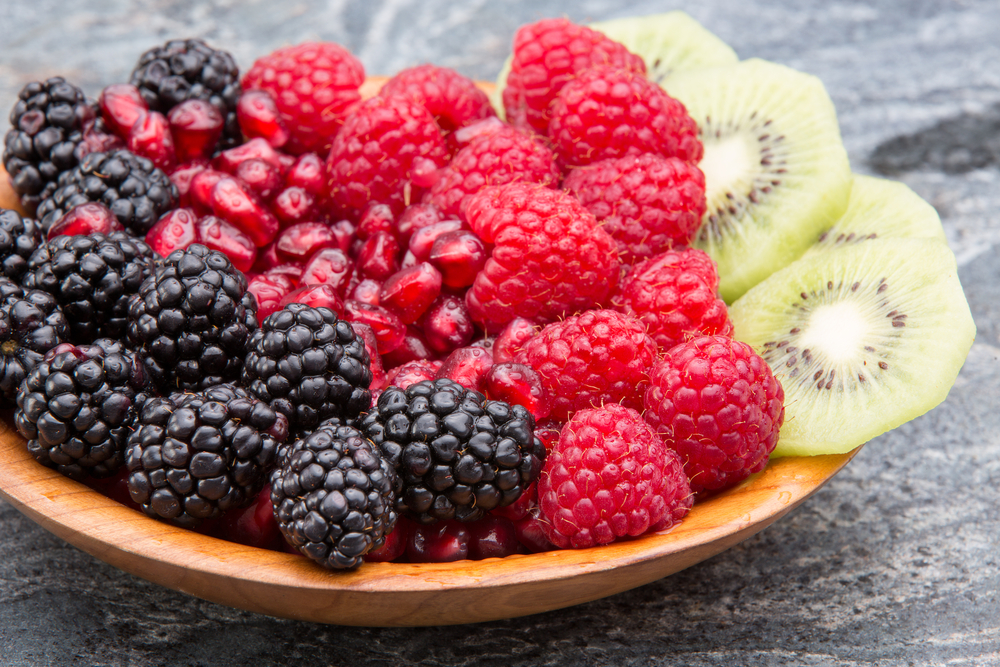 A bowl of blackberries, pomegranate seeds, raspberries and slices of kiwi fruit, fruit that has skin benefits.