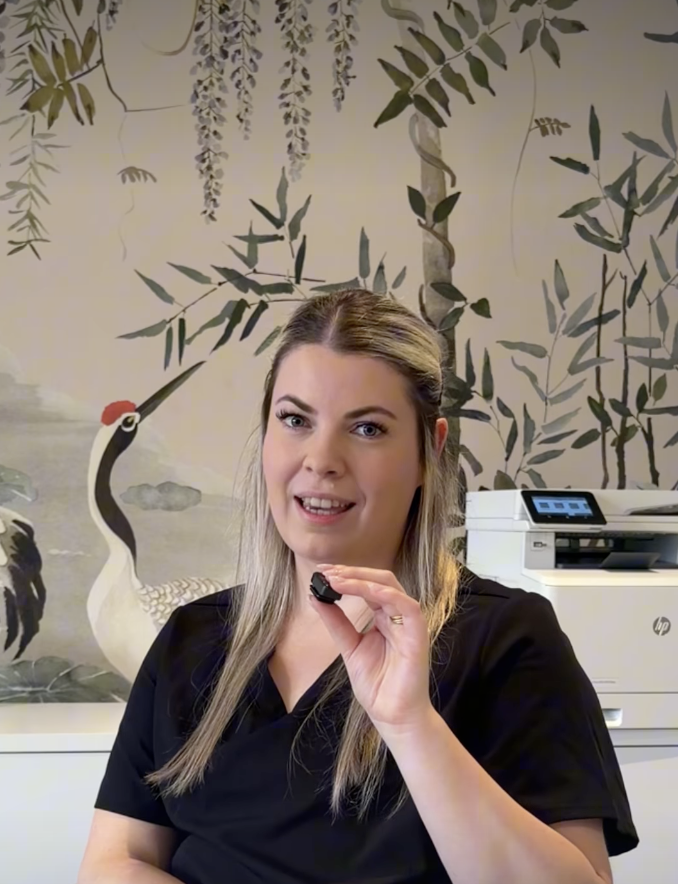 Nurse Ashleigh Robinson talks into a microphone about injectables in Pulse Aesthetic's clinic with birds and leaves wallpaper in the background.