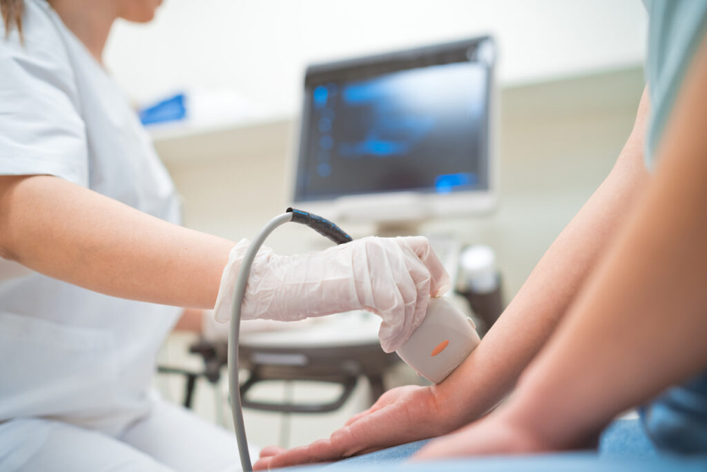 An ultrasound is being done on a patient's wrists as she turns her hands out.