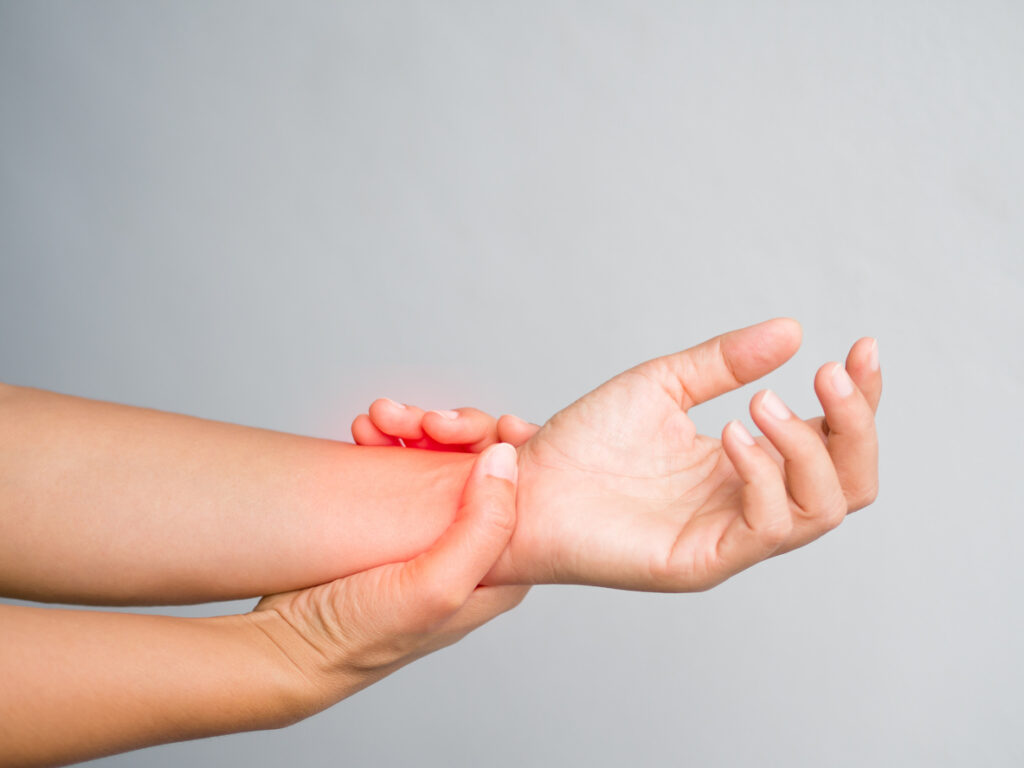 Woman supports her broken wrist with her other hand, both hands are on a plain background. She will need an ultrasound and X-ray.